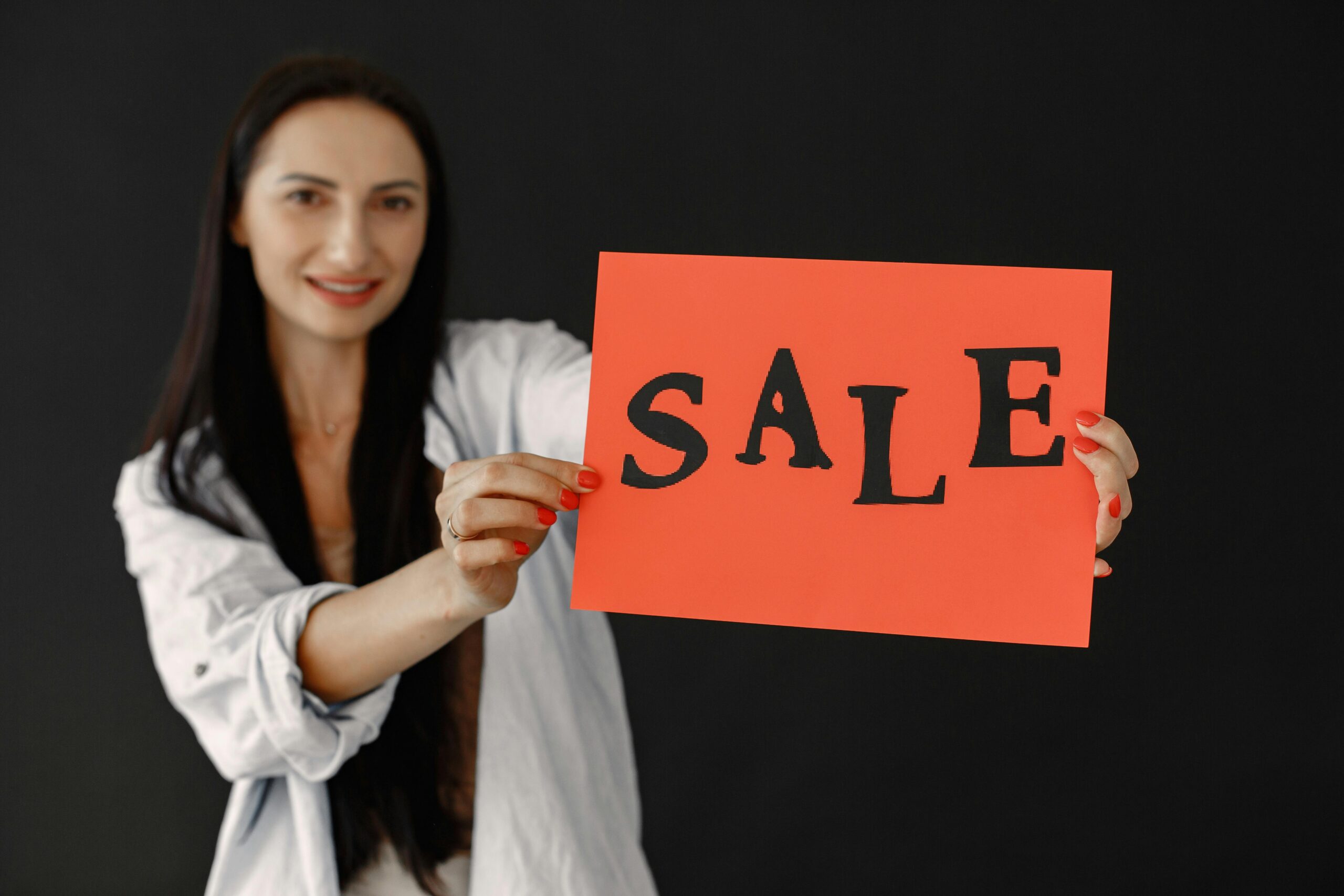 Portrait of a smiling woman holding a red sale sign in a studio setting, perfect for promotional use.