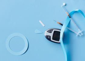 Flat lay of a diabetes monitoring kit with syringes and glucose meter on a blue background.